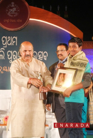 Dharmendra, Tribal Boy  receiving  the best Child Artiste  award from Maheswar Mohanty, Minister of Culture, Govt. of Odisha at Utkal Mandap on February 6, 2014 . Dr. Arabinda Padhi, Commissioner-cum- Secretary, Department of Culture, Govt. of Odisha looks on