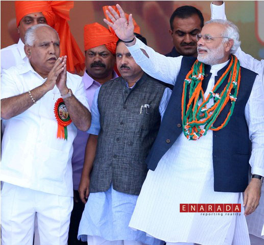 Narendra Modi waving to the crowd on his arrival at 'Bharata Gellisi' rally in Davangere.  Former CM B.S.Yeddyurappa and BJP state president Prahlad Joshi looks on